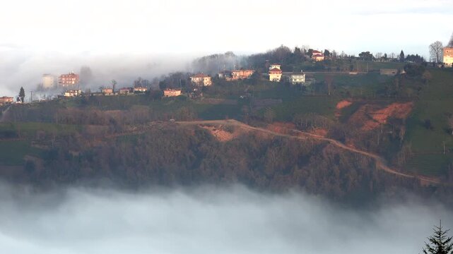 Rize Turkey village mosque rises above hillside homes beneath misty mountain clouds. Minaret, rural settlement, and green slopes create Black Sea cultural landscape.