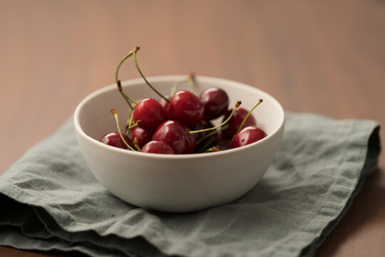 ripe cherries in white ceramic bowl on linen napkin