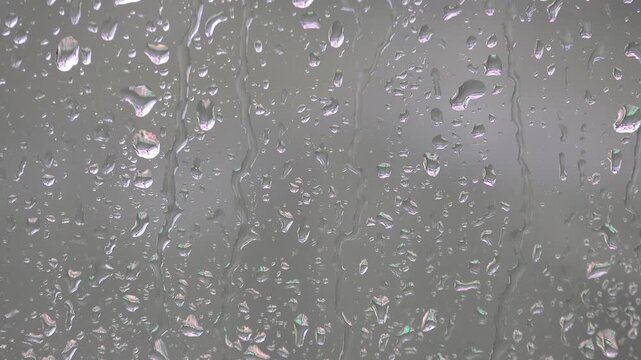 Rain droplets stream across foggy window glass, creating a wet surface with moody atmosphere. Condensation and blurred sky form a melancholic backdrop through misted panes and rainy texture.