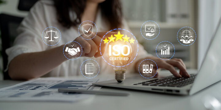 Business Professional Using Laptop with ISO Certified Lightbulb Icon and Graphs for Quality Management and Compliance Strategy Development. Glyphic.