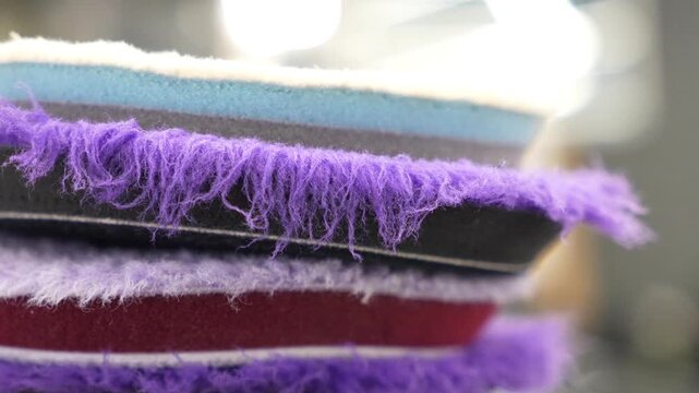 Close up of a stack of professional car detailing buffing pads. Multicolored wool and microfiber polishing wheels for electric dual action orbital machines in a garage auto workshop service station.