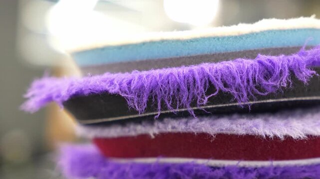 Close up of a stack of professional car detailing buffing pads. Multicolored wool and microfiber polishing wheels for electric dual action orbital machines in a garage auto workshop service station.