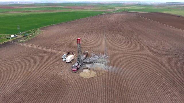 Aerial view shows water well drilling rig working farmland for artesian groundwater extraction. Industrial machine bores into agricultural soil, supporting irrigation and rural development.