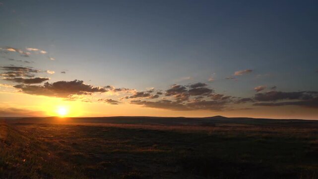 Mongolia steppe sunset spreads orange light across treeless grassland and distant dark mountains. Twilight afterglow colors empty prairie, casting amber evening tones over remote open country.