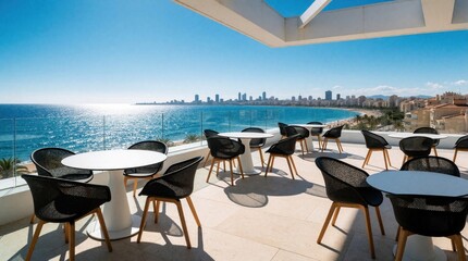 Obraz premium Modern rooftop terrace with white tables, black chairs overlooks blue sea. Luxury hotel balcony offers panoramic city skyline view. Sunny coastal patio provides outdoor seating for cafe bar during