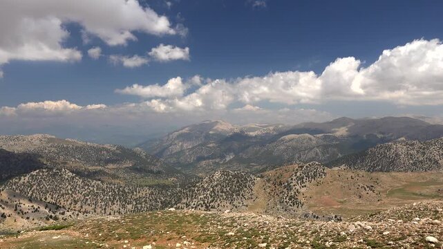 Timelapse shows vast mountains with sparse forests and deep valleys under moving sunlight. Fixed view reveals layered ridges, mixed climate zones, warm temperate scenery under clear weather.