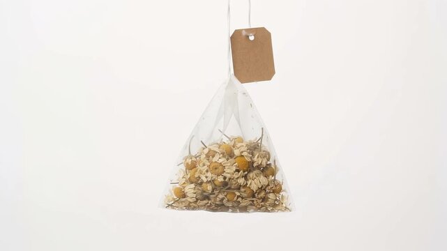 Chamomile herbal tea bag with blank craft paper tag. Pyramid mesh tea sachet with dried flowers. Organic infusion on white background.
