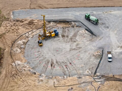 Foundation construction of a wind turbine with crawler tracks, deep vibrators, wheel loaders and concrete mixers on a construction site for soil improvement, viewed from a bird's-eye view