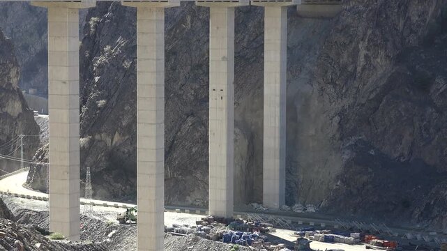 Modern mountain viaduct crosses a rocky valley on tall concrete pillars. Cliff tunnel and elevated span highlight rugged transport engineering.