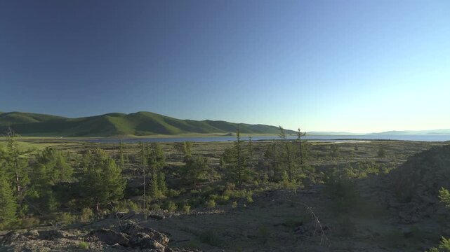 Panoramic view of Central Asia lakeside basalt plain with frozen lava rocks and volcanic terrain. Solidified magma meets quiet water, barren steppe, remote dawn atmosphere, earth science.