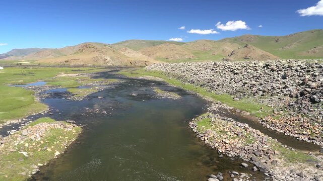 Mongolia arid river landscape cuts through rocky plains, dry mountains, remote wilderness. Barren valley terrain surrounds flowing water, steppe scenery, vast natural solitude.