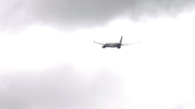 Commercial passenger airplane climbing and flying through white overcast clouds in the sky, telephoto tracking shot