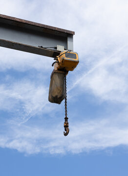 Industrial chain hoist with lifting hook against cloudy sky.