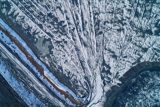 Snowy eroded slag heap slopes with frozen drainage stream and dark mineral veins, top view aerial shot