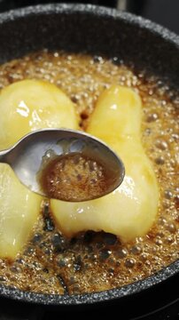 Liquid caramel pours over pear pieces in frying pan. Warm fruit topping adds sweet flavour and golden glaze to autumn breakfast. Serve caramelized pears with pancakes, waffles, oatmeal or porridge.