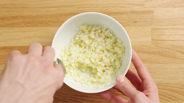 Spoon stirs diced pear in white bowl on wooden table. Juicy fruit pieces make fresh salad with apples, grapes, berries or yogurt. Light pear snack suits breakfast, lunchbox, picnic or healthy dessert.