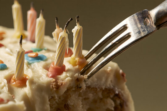 Fork cutting into a birthday cake with burnt out candles still in it