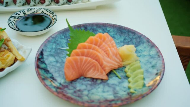 Close-up of sliced salmon sashimi with a shiso leaf, wasabi and pickled ginger on a decorative plate