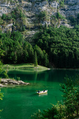 A small boat on the emerald green waters of Seealpsee lake with a traditional alpine chalet and tall pine tree, Alpstein massif, Appenzell Alps, Switzerland © Roman
