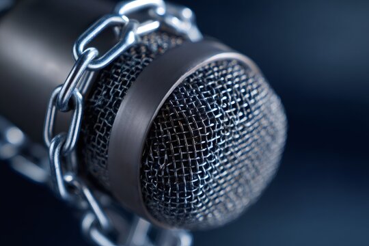 Microphone wrapped in a chain on a dark background. Censorship and freedom of speech concept. Silenced voice or restricted press metaphor