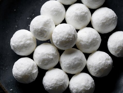 White camphor balls rest on dark surface. These aromatic spheres prevent moth damage to clothing and offer a pleasant scent. Used in closets and drawers for protection.