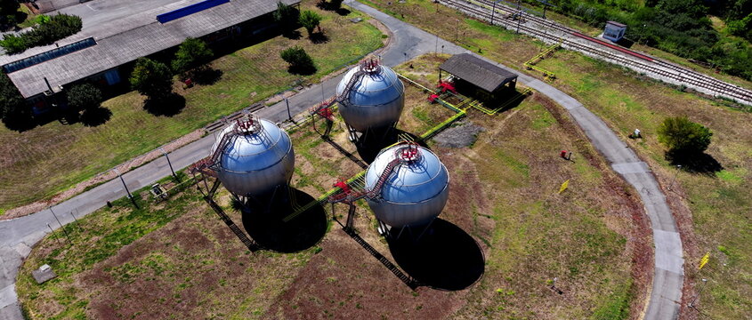 Aerial view of spherical industrial gas storage tanks situated in an open field near a railway line and industrial buildings in Belgrade, City of Belgrade, Serbia.