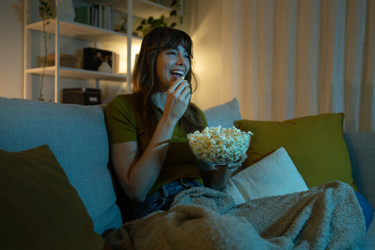 Woman watching movie at home laughing and eating popcorn