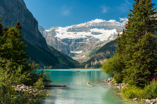 Lake Louise summer landscape with tourists canoeing on turquoise water under Victoria Glacier. Banff, Alberta, Canada.