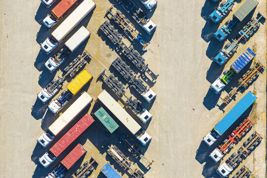 Aerial view of a busy logistics terminal with numerous semi-trucks, shipping containers, and trailers parked in organized rows at the port of La Spezia, Liguria, Italy.