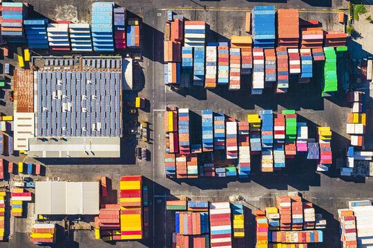 Aerial view of the busy container terminal in the port of La Spezia featuring rows of colorful shipping containers and a large warehouse with solar panels on the roof in La Spezia, Liguria, Italy.
