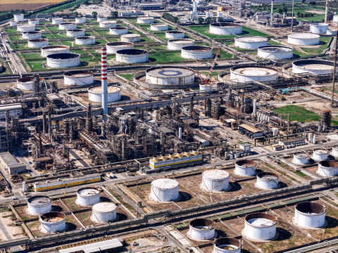 Aerial view of the Eni oil refinery with numerous large storage tanks, complex processing units, and industrial infrastructure in Sannazzaro de' Burgondi, Lombardy, Italy.