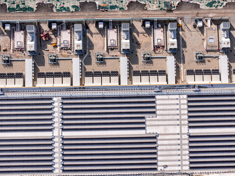 Aerial view of the Noviglio Data Center, showcasing rows of cooling units, technical infrastructure, and large solar panel arrays on the roof in Noviglio, Lombardy, Italy.
