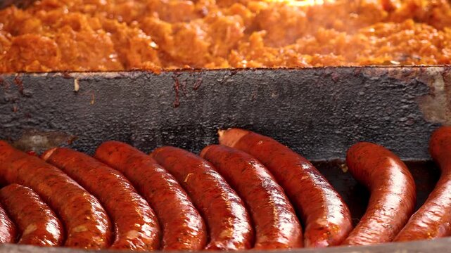 Grilled polish sausages frying on large pan at street food market