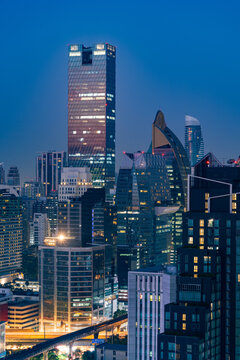 Aerial view of illuminated skyscrapers at twilight with a skytrain track visible below in Bangkok, Thailand.