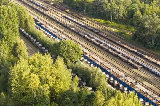 Aerial view of freight trains carrying steel coils on specialized wagons through a lush forest landscape in Poland.