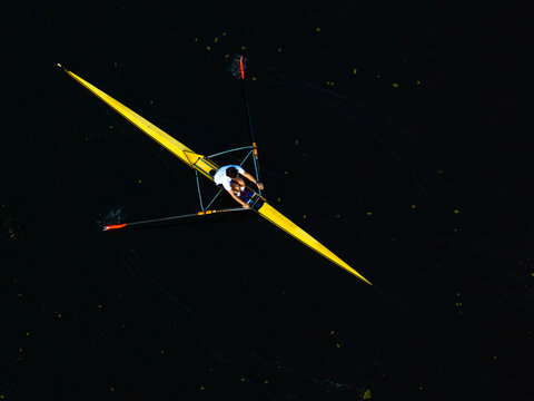 Aerial view of a person rowing a yellow scull boat on dark water in Poland.