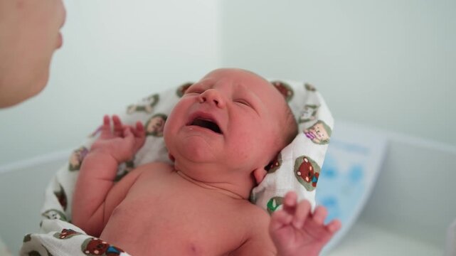 Close-up of a crying newborn baby held in his mother's arms, as she gently watches over and comforts him, capturing a tender moment of maternal care and early infancy