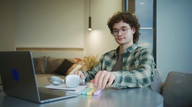A student tidies up his desk in a cozy apartment, gathering books and supplies with a laptop after long hours of study and concentration
