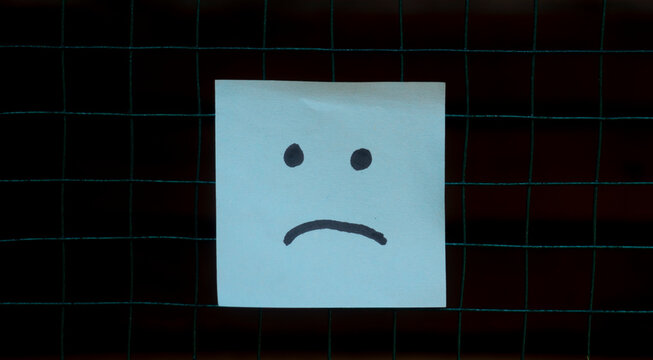 Sad Face Sticky Note on Dark Grid Background Concept, representing sadness, loneliness, negative emotions, mental health, or emotional distress with copy space.