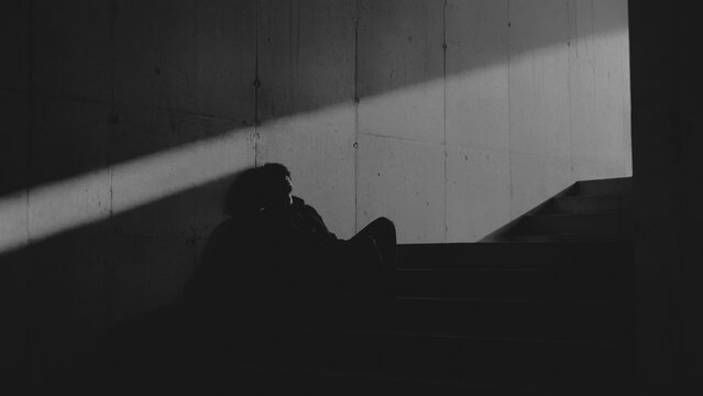 Silhouetted person sitting on concrete stairs in dramatic diagonal light for solitude, contemplation and urban mood concepts