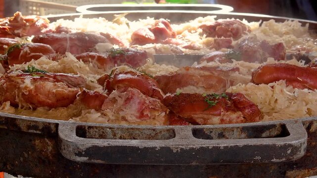 Huge pan with steaming pork knuckle sauerkraut and sausages at street market