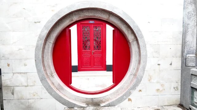 Traditional moon gate entrance and red wooden lattice doors at a historic Chinese temple in Cholon, Ho Chi Minh City, Vietnam