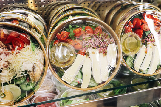 Prepared salads in clear bowls contain tomatoes greens sprouts cheese and dressing under plastic lids. Fresh takeaway meal background with vegetables ready portions and convenient cold food.