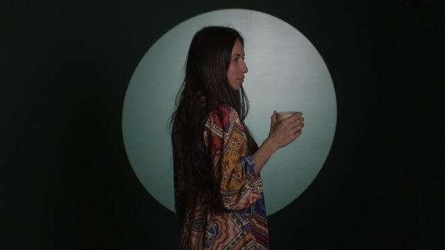 Trendy woman takes sip of drink in front of circular light rotating into view - abstract young adult woman