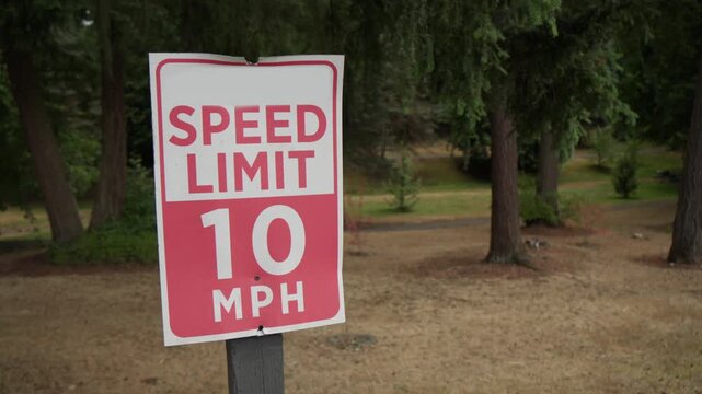  Red and white 10 mph speed limit sign beside a park road with trees. Traffic safety, low speed zone, and driving regulation concept.