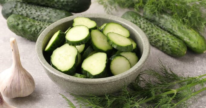 Sliced cucumbers in bowl, dill and garlic on gray table, closeup. Camera zooming in