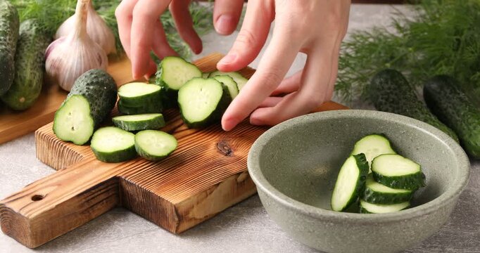 Woman putting sliced cucumber into bowl at gray table, closeup