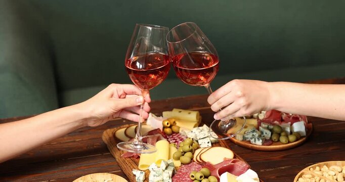 Friends clinking glasses of wine at table indoors, closeup