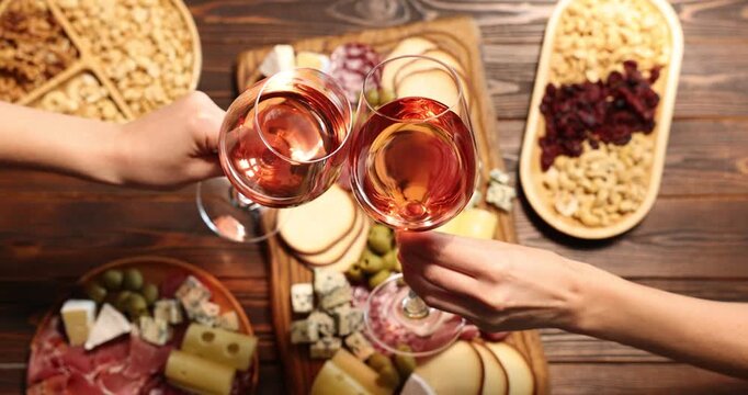 Friends clinking glasses of wine at wooden table indoors, top view