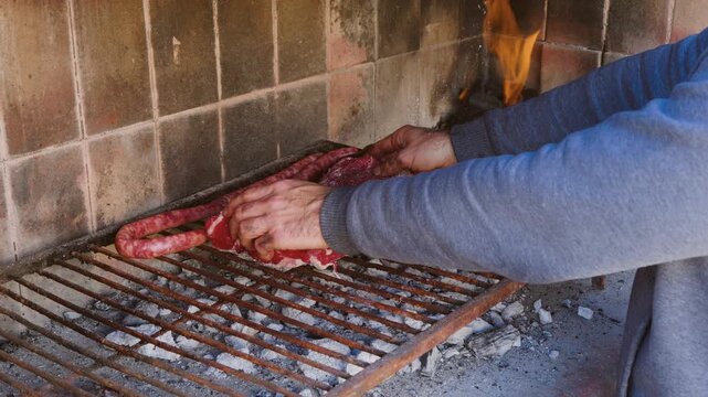 Unrecognizable Man Placing Raw Beef on a Traditional Brick Parrilla Next to Chorizo Sausages, Argentine Asado, 4K